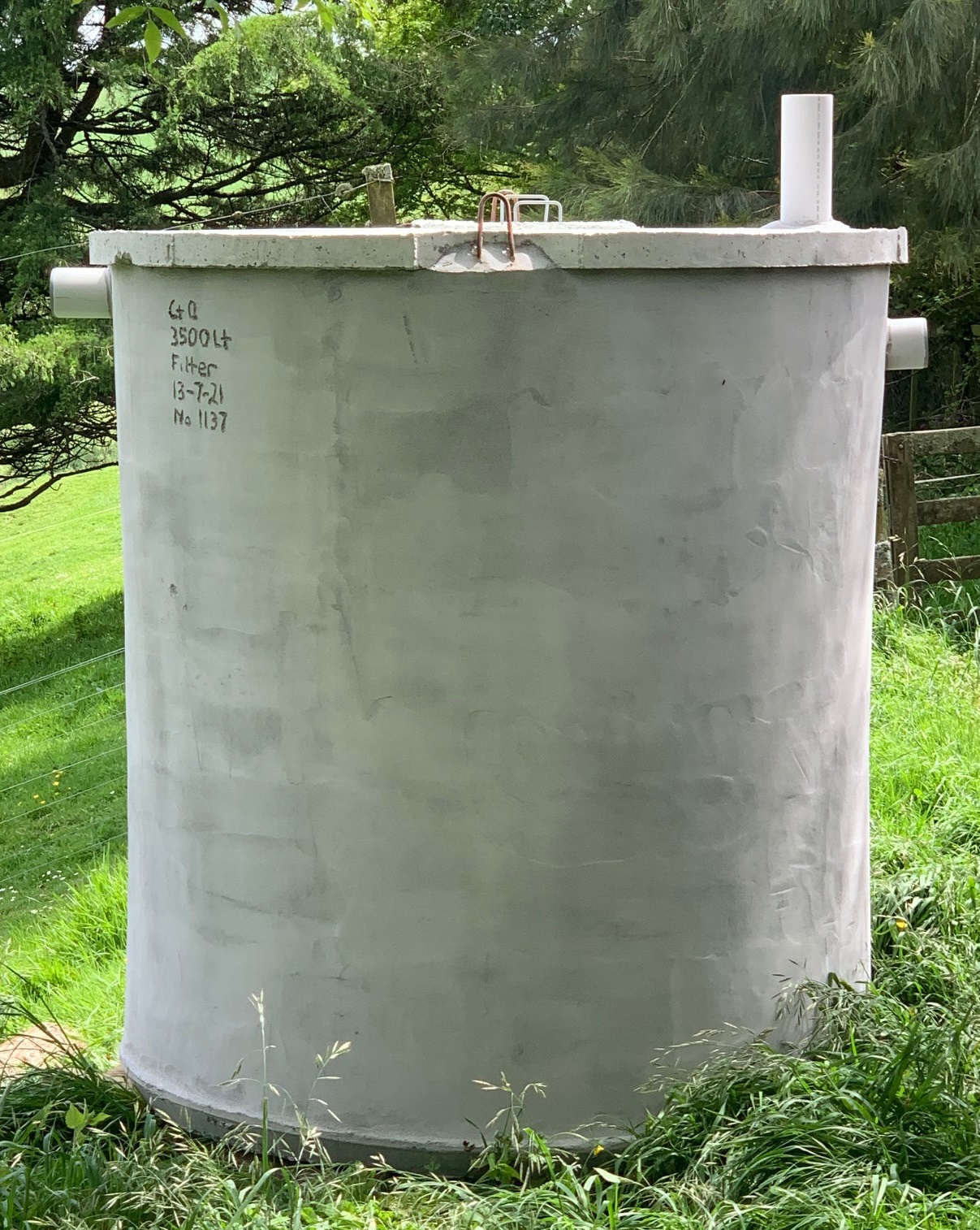 Tall cylindrical concrete septic tank standing in grass